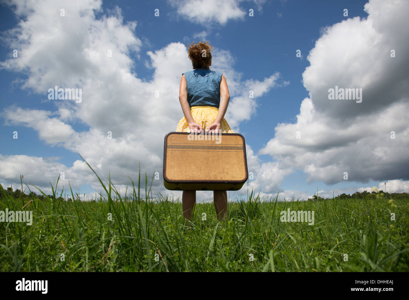 Teenage girl holding suitcase in field Banque D'Images