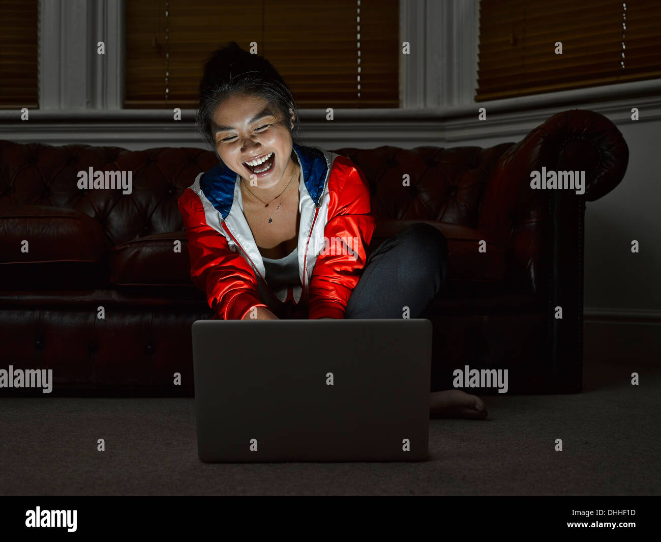 Young woman sitting on floor laughing at digital tablet Banque D'Images