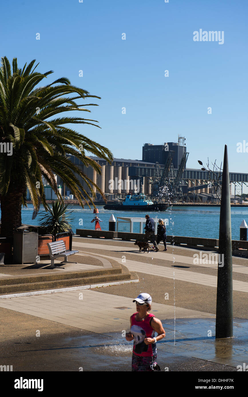 Les personnes bénéficiant d'aménagement du front de mer de Newcastle avec installations de chargement des navires en arrière-plan. Banque D'Images