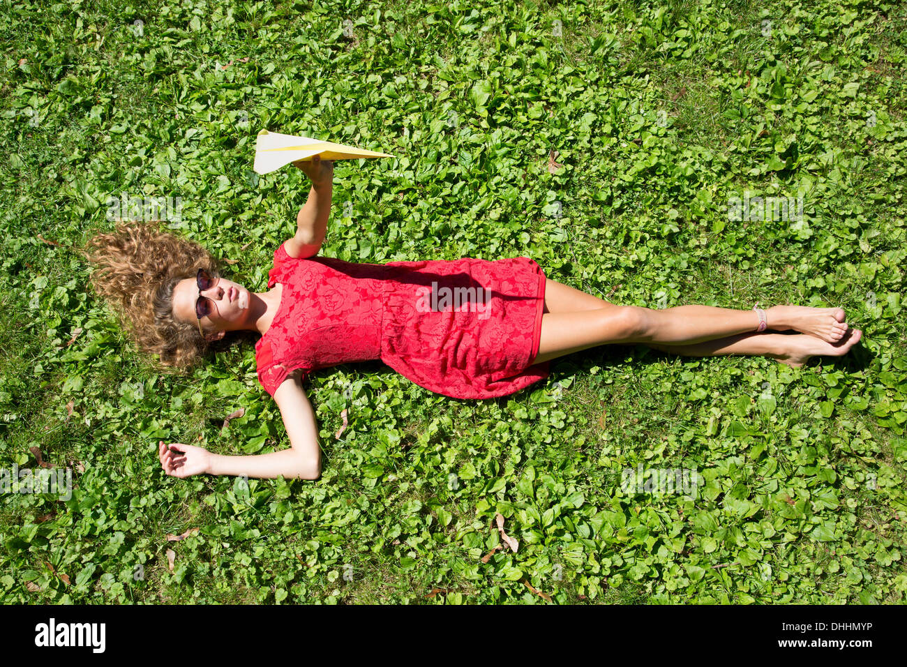 Teenage girl lying on grass holding paper aeroplane Banque D'Images