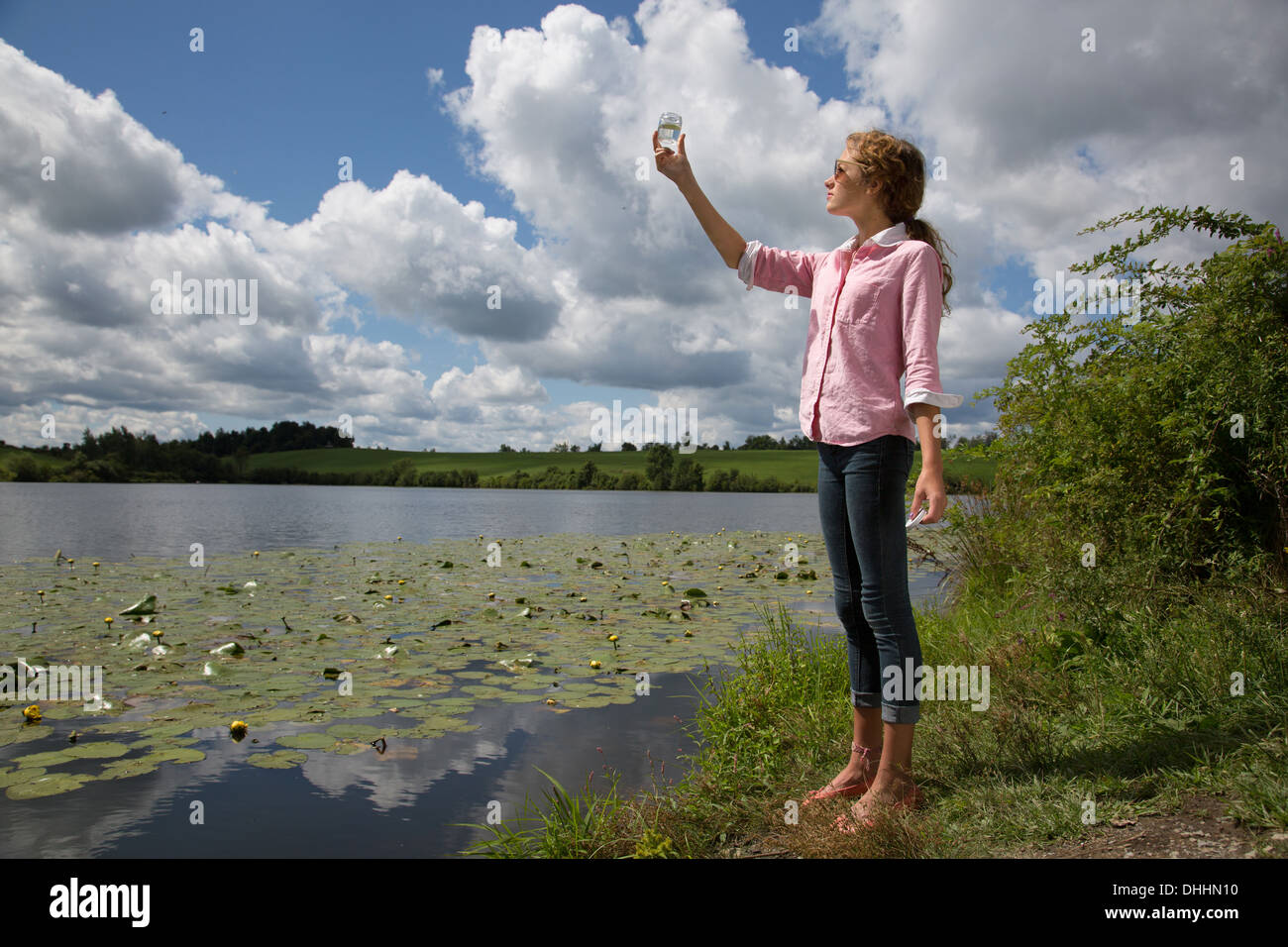 Teenage girl holding up bocal en verre à côté du lac Banque D'Images