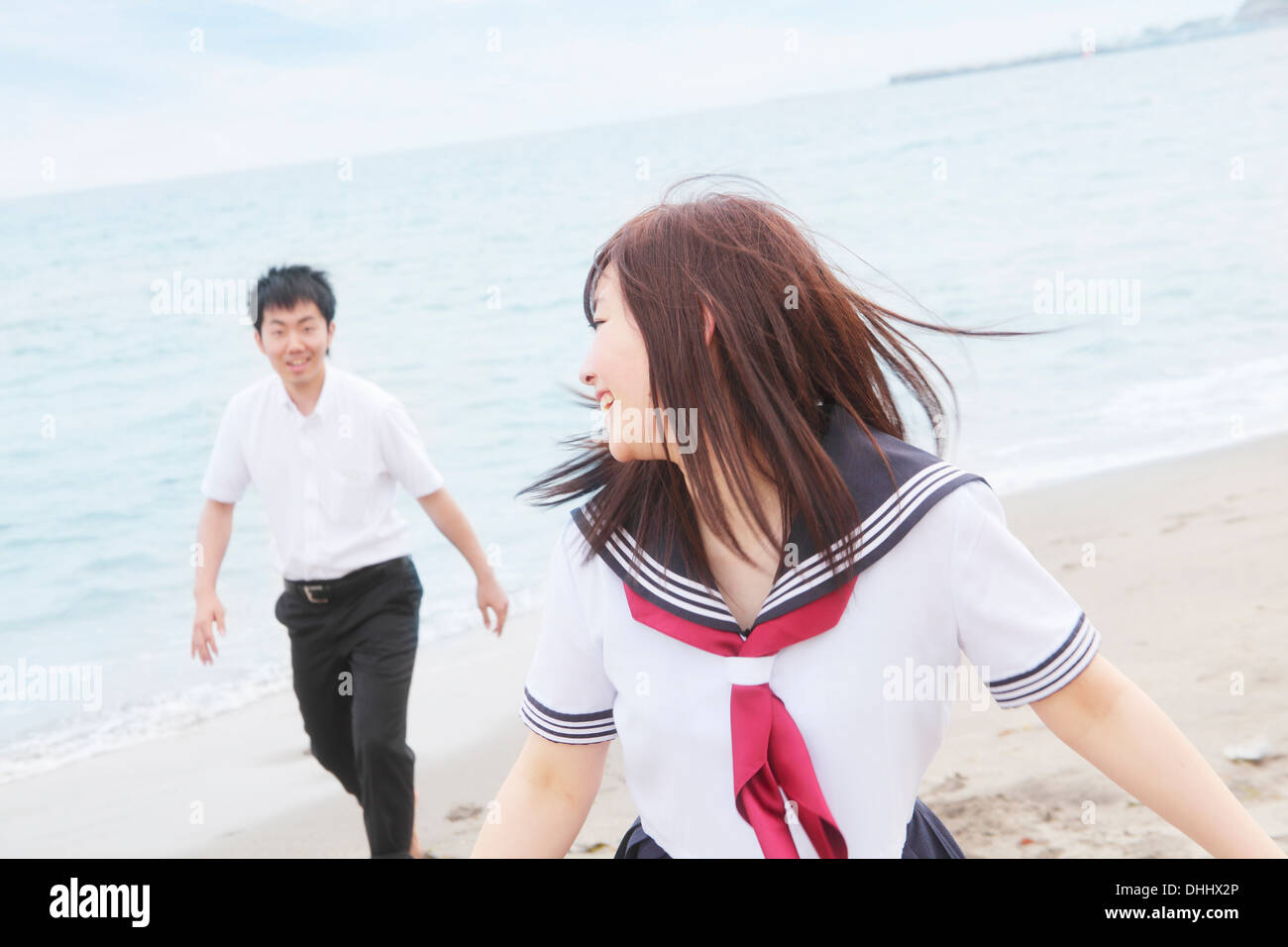 Young couple wearing school uniform running on beach Banque D'Images