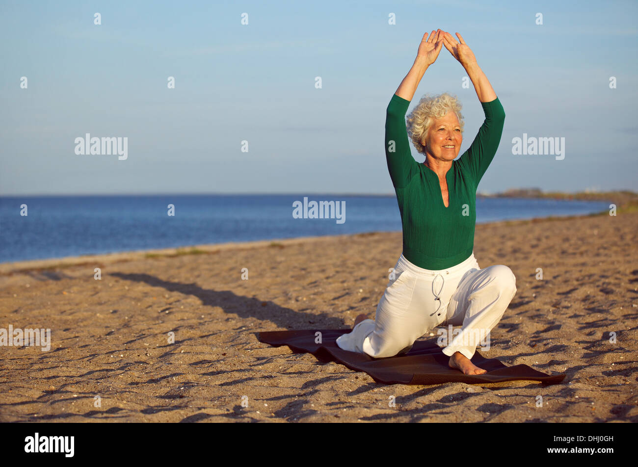 Happy senior woman practicing yoga sur la plage de sable. Mature Woman stretching les jambes et les bras sur le bord de la mer. Banque D'Images