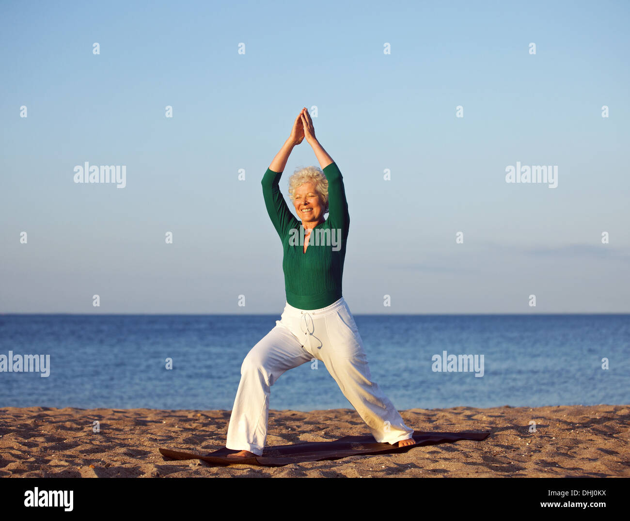 Senior woman stretching contre fond de plage. Mature Woman exercising on sandy beach in morning Banque D'Images
