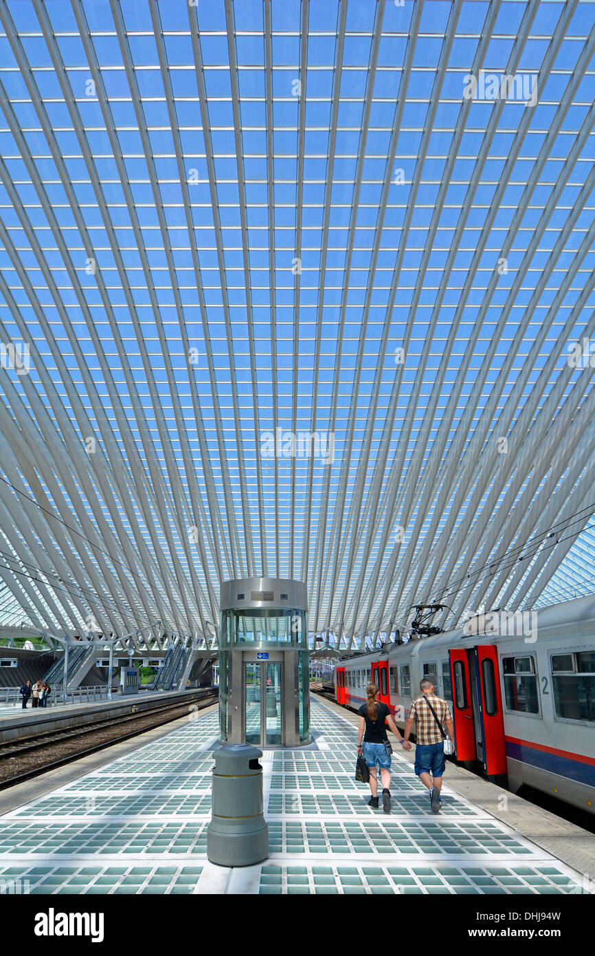 Man & woman couple marche main dans la main le long de la plate-forme de la gare Liège Belgique ci-dessous bâtiment moderne en verre bleu ciel été jour plafond Banque D'Images
