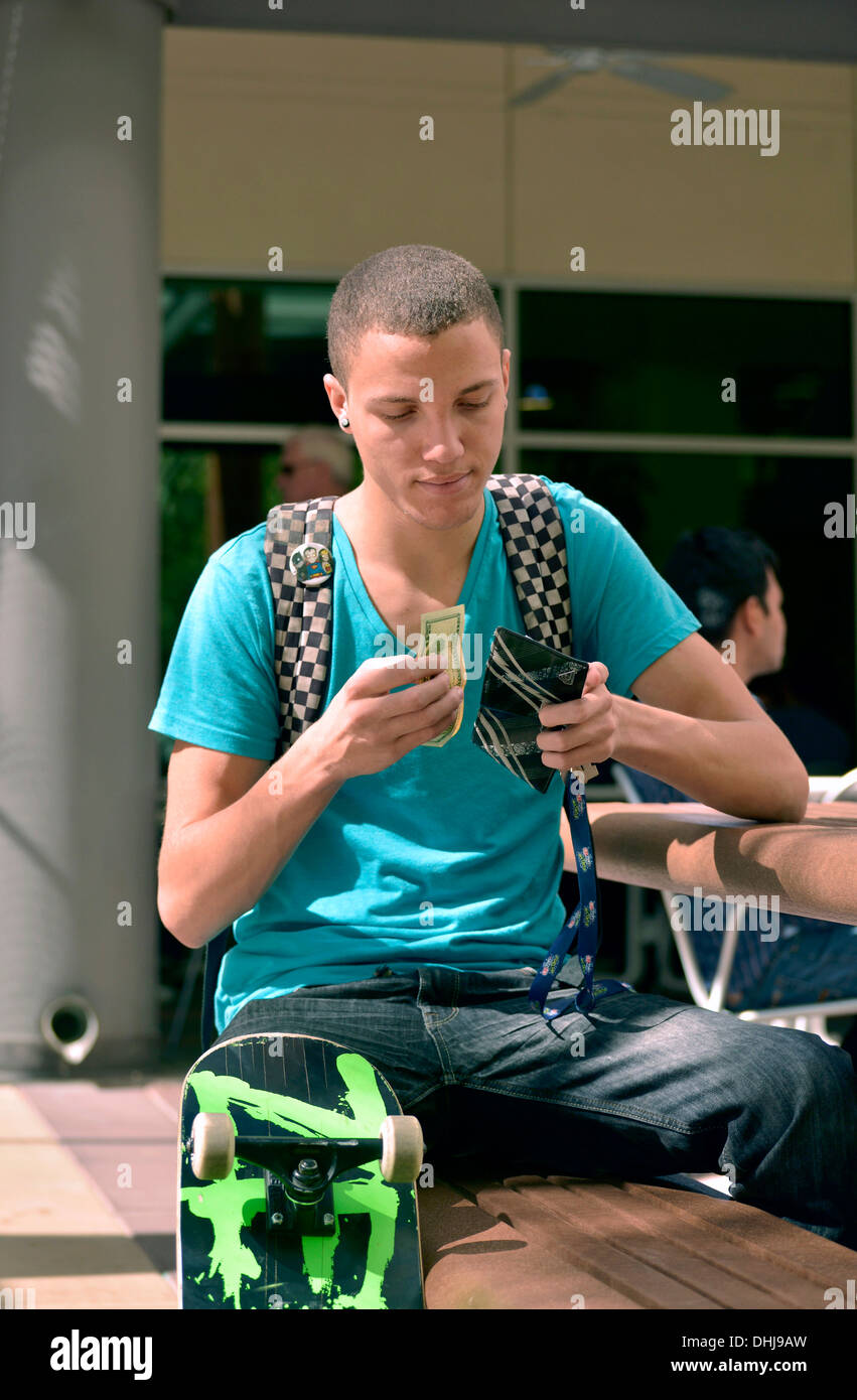 Un jeune homme avec un porte-monnaie et de l'argent sur un campus universitaire. Banque D'Images