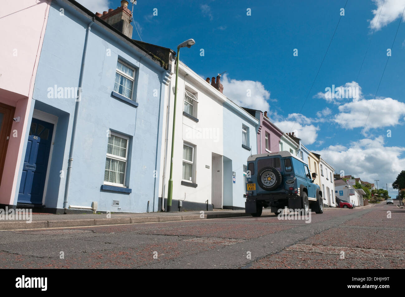 Land Rover Defender en descendant le long de la rue peint pastel des maisons mitoyennes à Paignton, Devon, UK. Banque D'Images