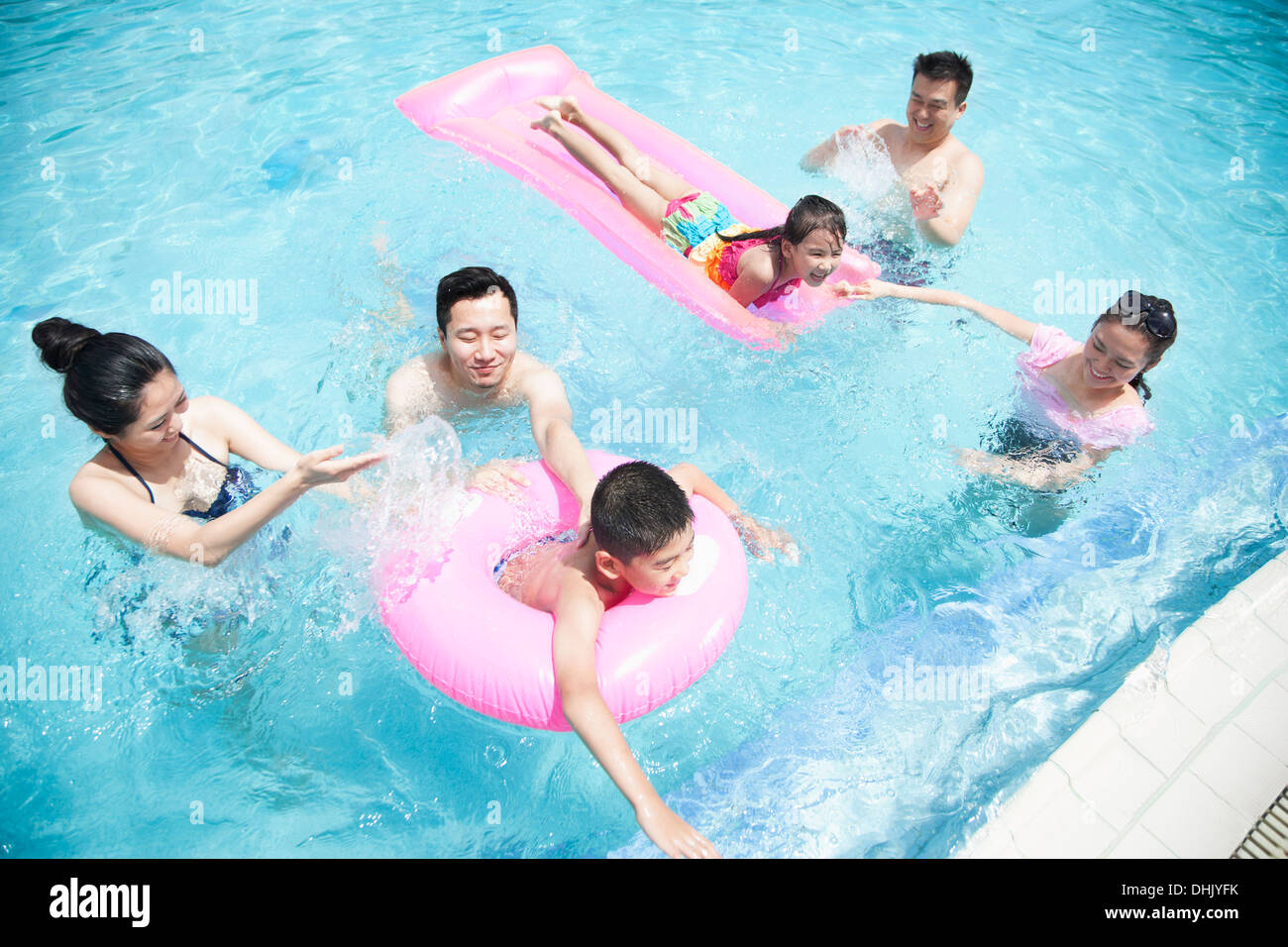 Famille et amis jouant dans l'eau à la piscine avec des tubes gonflables Banque D'Images