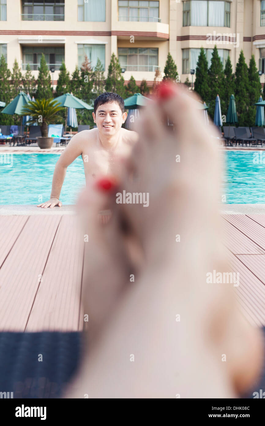 Close up of young woman's pieds sur le bord de la piscine, l'homme hors de l'eau dans l'arrière-plan Banque D'Images