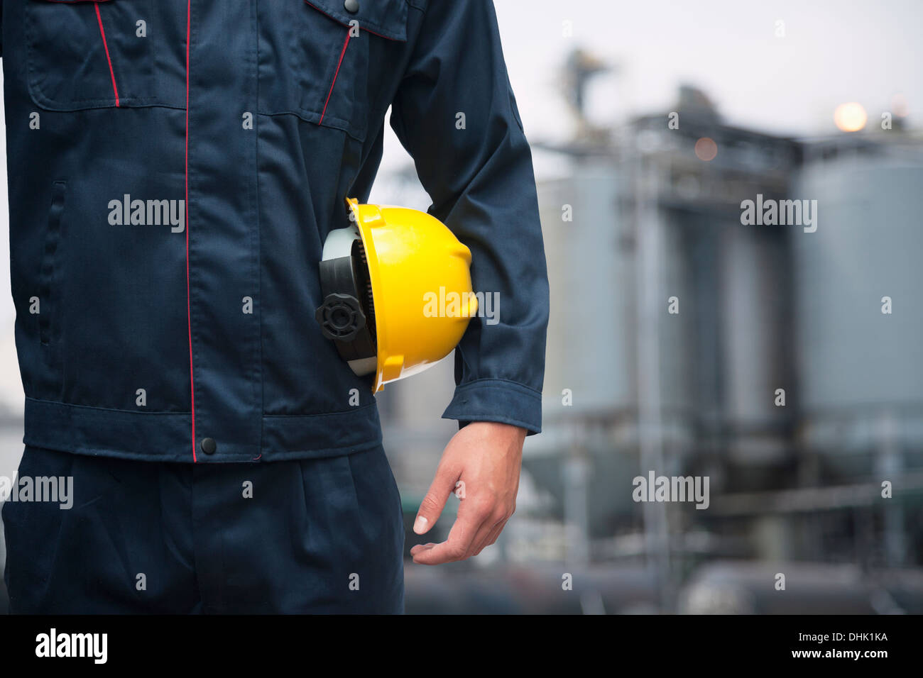 Portrait de jeune travailleur ayant un casque jaune à l'extérieur avec l'usine à l'arrière-plan Banque D'Images