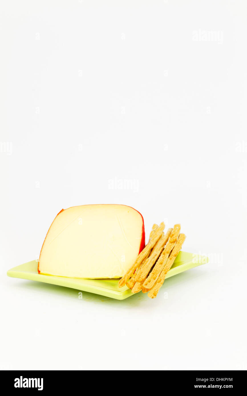 Tranche de fromage jaune avec de l'écorce rouge placé avec bâtonnets de pain sur la plaque, carré vert contre l'arrière-plan blanc. Banque D'Images
