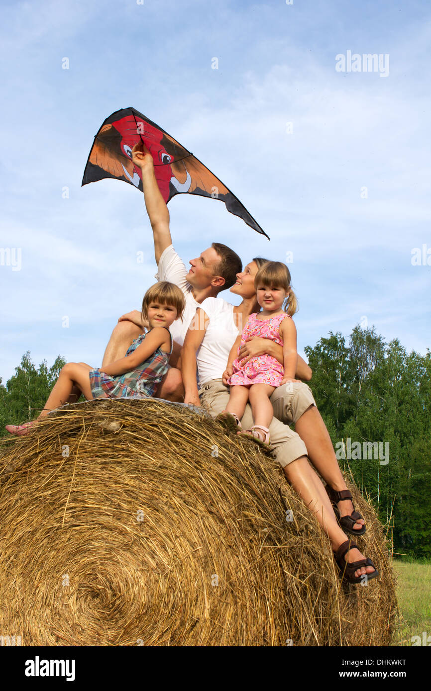 L'heureuse famille à cheval sur hay flying kite. Banque D'Images
