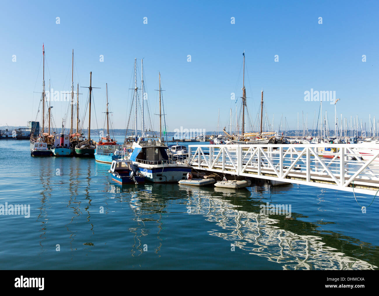 Passerelle jetée blanche menant à bateaux et yachts dans la marina avec ciel bleu et réflexions Banque D'Images