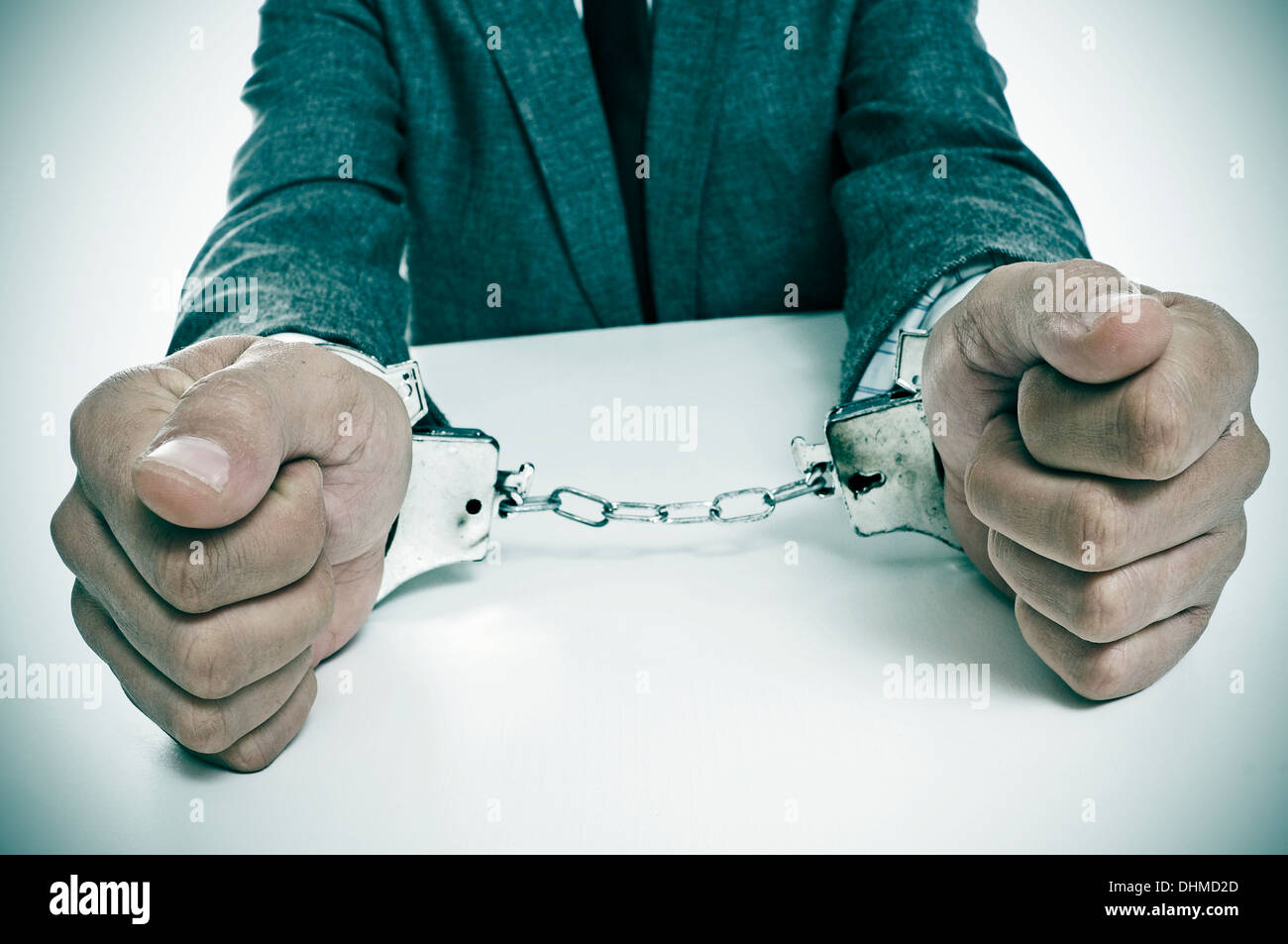 Un homme portant un costume assis dans un bureau, avec des menottes à ses poignets Banque D'Images
