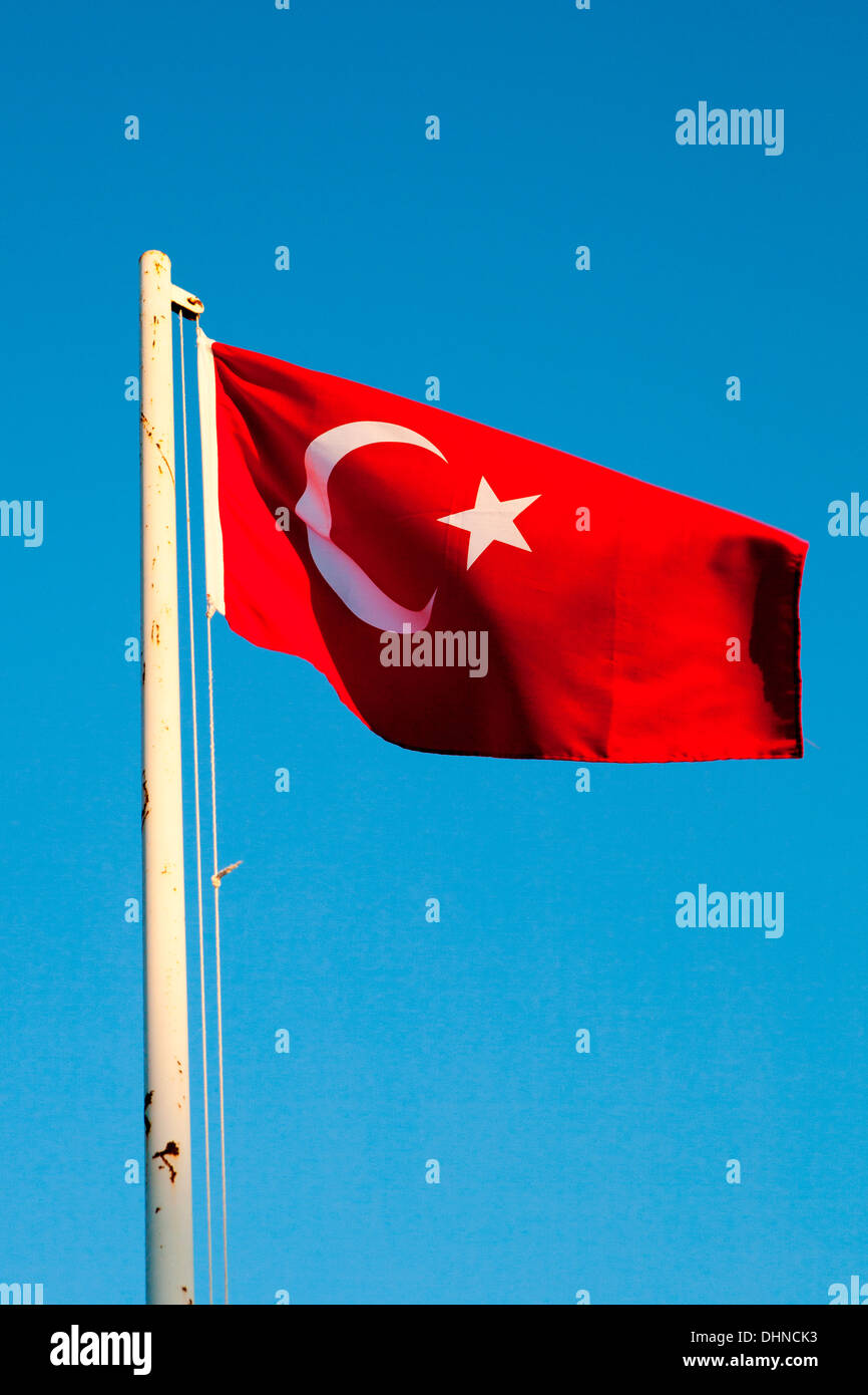 Le drapeau national de la Turquie voler contre un ciel bleu méditerranéen dans le sud de la Turquie. Banque D'Images