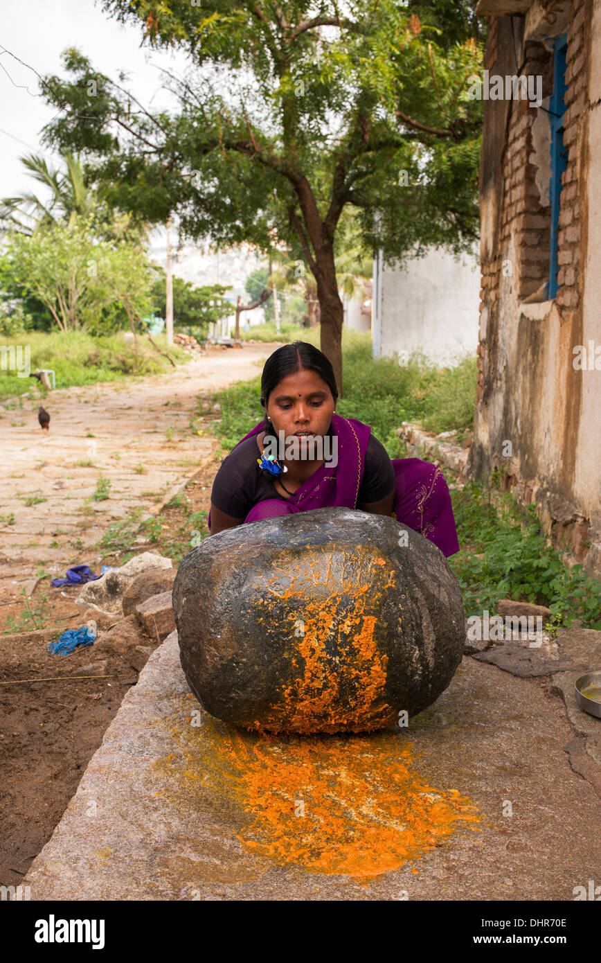 Femme indienne en utilisant une pierre pour moudre des ingrédients pour faire l'extérieur de son chutney maison de village rural. L'Andhra Pradesh, Inde Banque D'Images