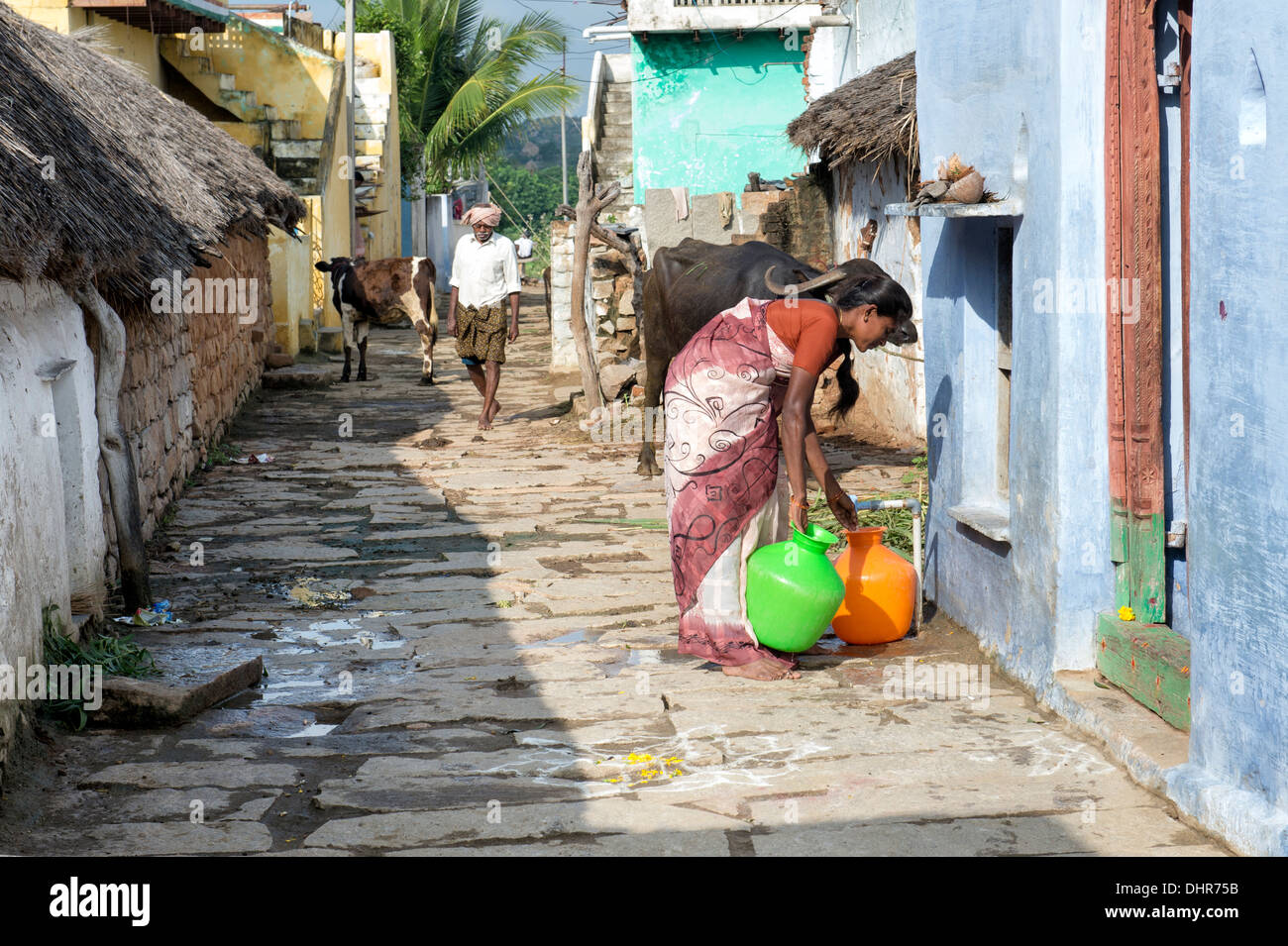 Femme indienne le remplissage des pots en plastique avec de l'eau d'un tube de mesure dans une rue village. L'Andhra Pradesh, Inde Banque D'Images