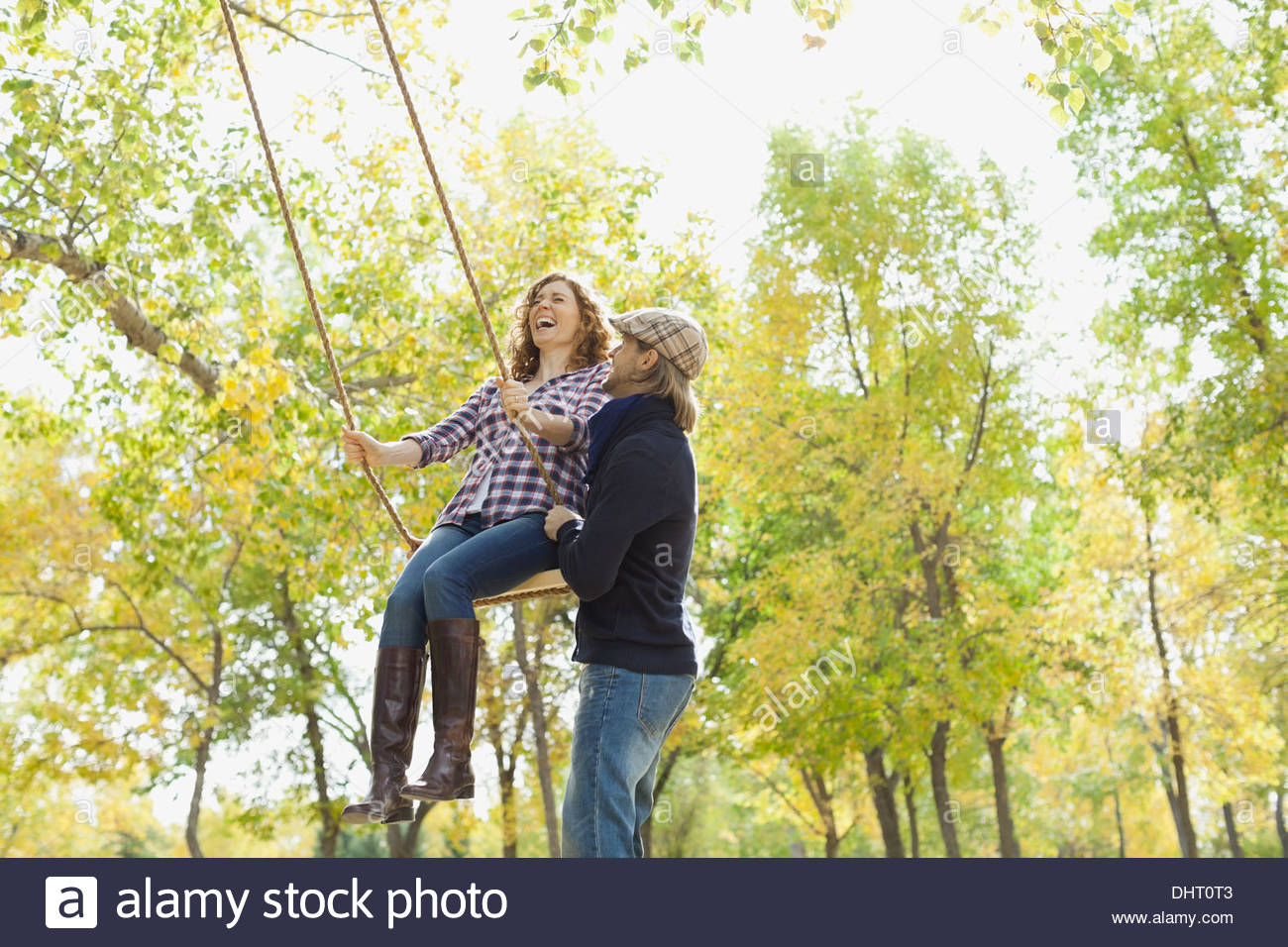 Mid adult man pushing woman on swing au parc en automne Banque D'Images