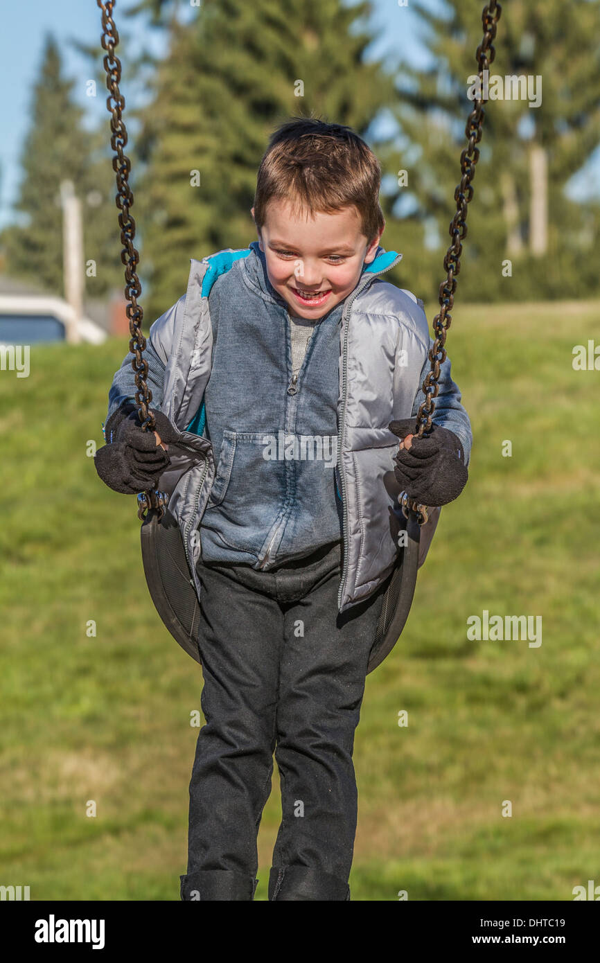 Parution du modèle, mignon, sourire, rire, garçon de 5 ans, de s'amuser dans l'aire de jeux en plein air, sur swing. Banque D'Images