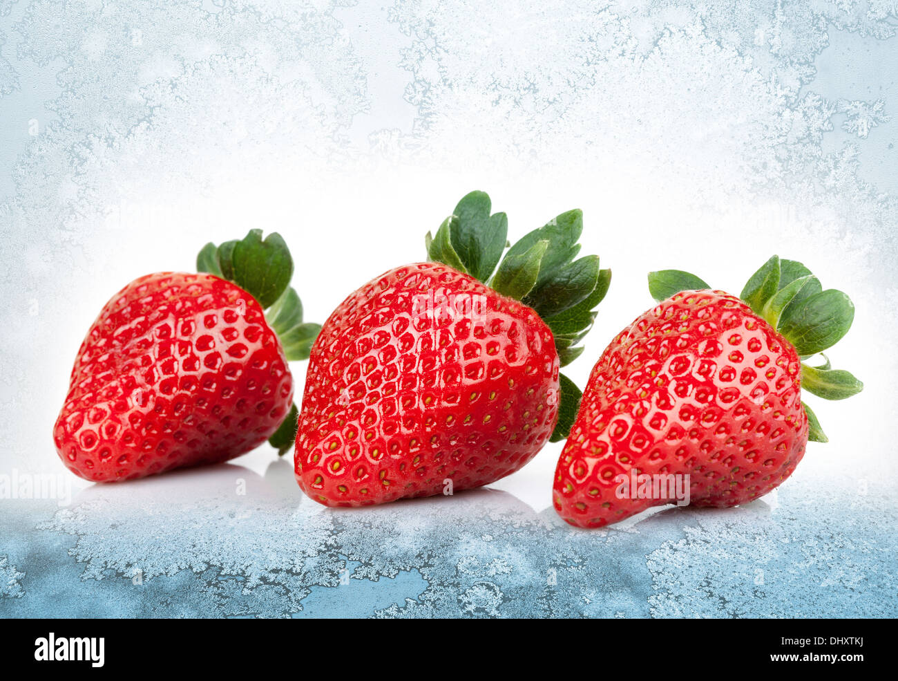 3 fraises fraîches jeter sur fond de glace bleu Banque D'Images