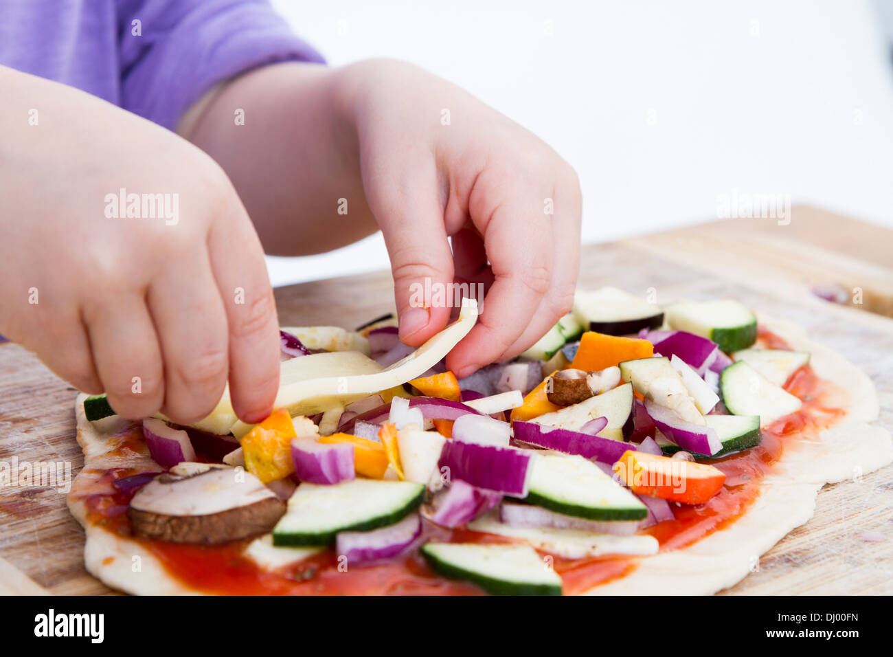 Les petites mains préparation de pizzas fraîches avec beaucoup de légumes Banque D'Images