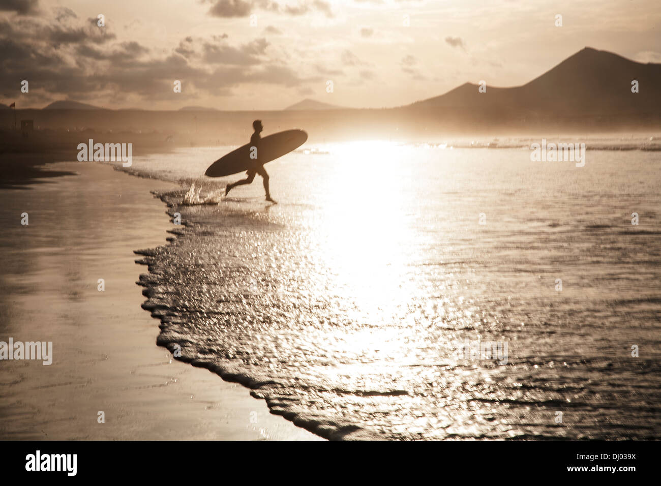 Un internaute passe dans la mer d'or à attraper le dernier des vagues avant le coucher du soleil. Banque D'Images