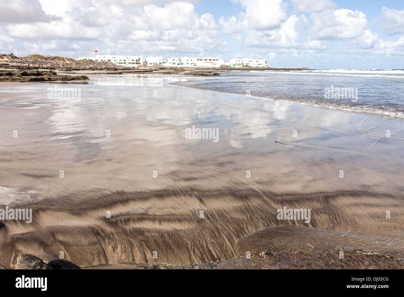 Vue sur la télévision étendue de la plage de Famara à vers la ville en arrière-plan. Le ciel nuageux se reflète clairement Banque D'Images