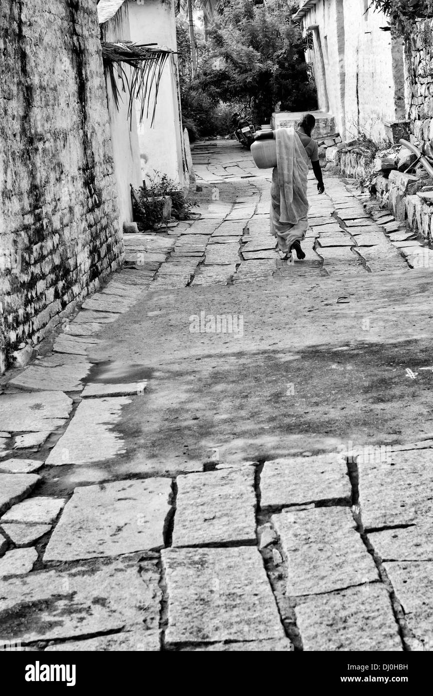 Femme indienne portant un pot en plastique avec de l'eau d'un tube de mesure dans une rue village. L'Andhra Pradesh, Inde. Noir et blanc. Banque D'Images