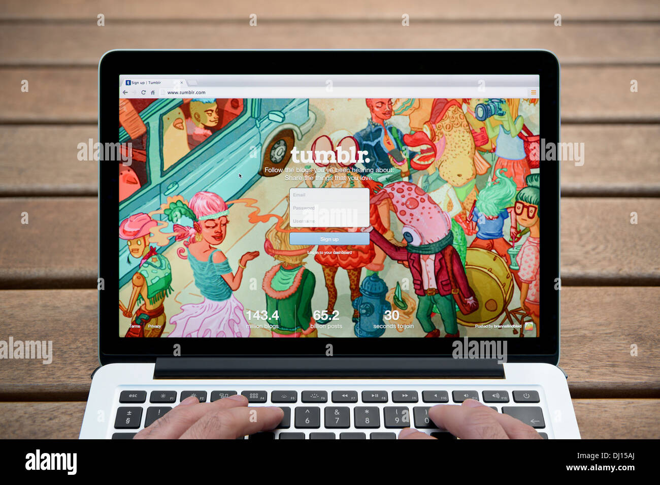Le Tumblr site sur un MacBook contre un banc en bois fond de plein air y compris les doigts d'un homme (usage éditorial uniquement). Banque D'Images