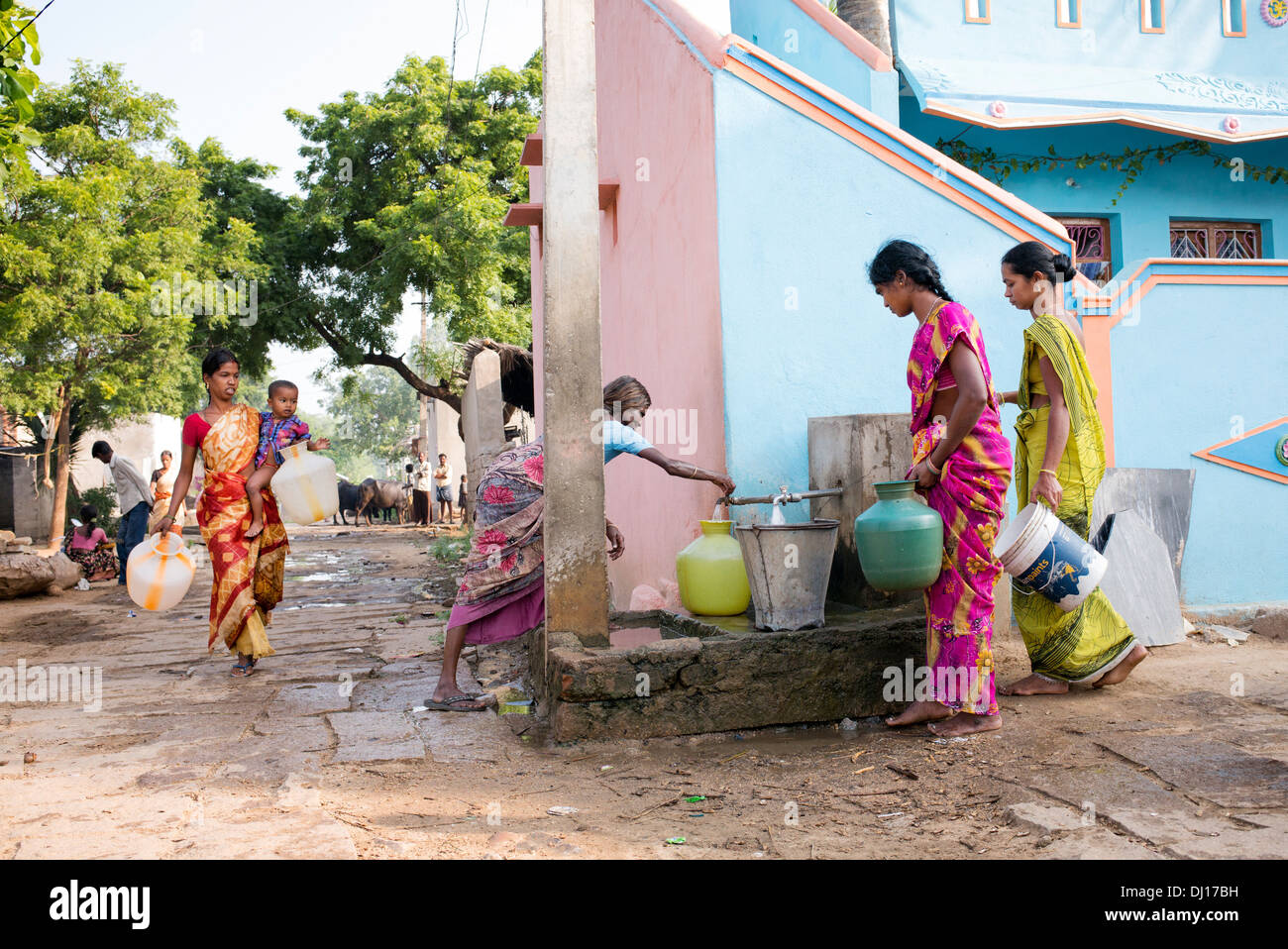 Les femmes indiennes le remplissage des pots en plastique avec de l'eau d'un tube de mesure dans une rue village. L'Andhra Pradesh, Inde Banque D'Images