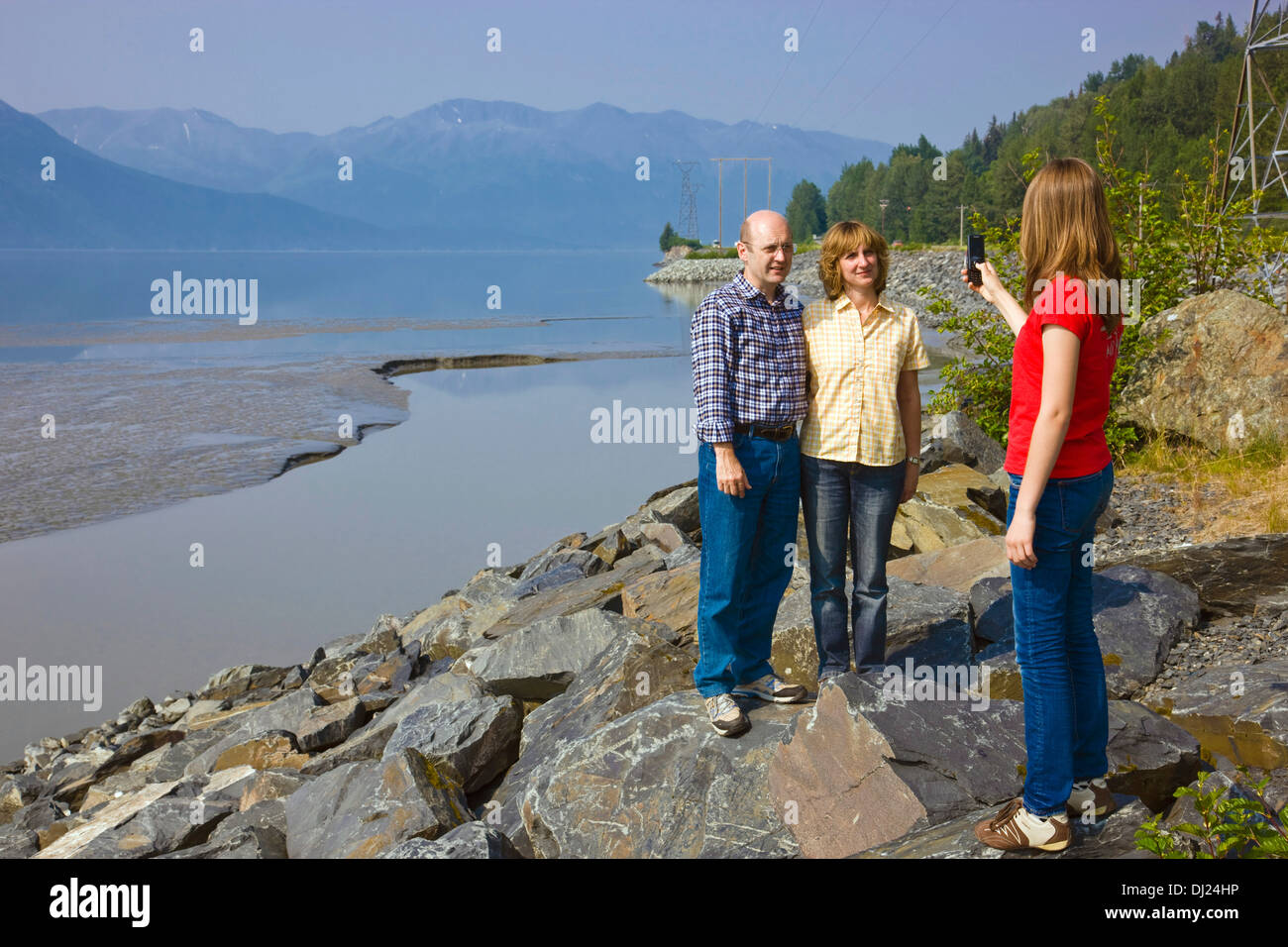 Fille adolescente en tenant un portrait de famille avec un téléphone cellulaire le long de Turnagain Arm, Kenai Mountains en arrière-plan, de l'Alaska Banque D'Images