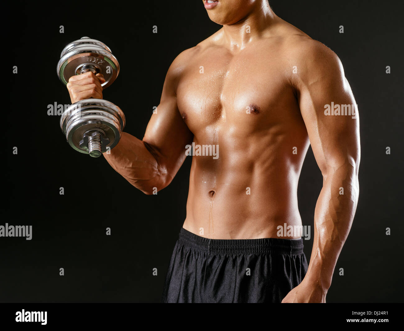 Photo d'un homme asiatique l'entraînement avec haltères et faire des biceps sur fond sombre. Banque D'Images