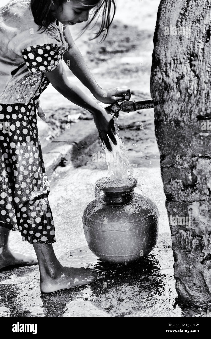 Indian girl remplissage d'un pot en plastique avec de l'eau d'un tube de mesure dans un village de l'Inde rurale. L'Andhra Pradesh, Inde. Noir et blanc. Banque D'Images
