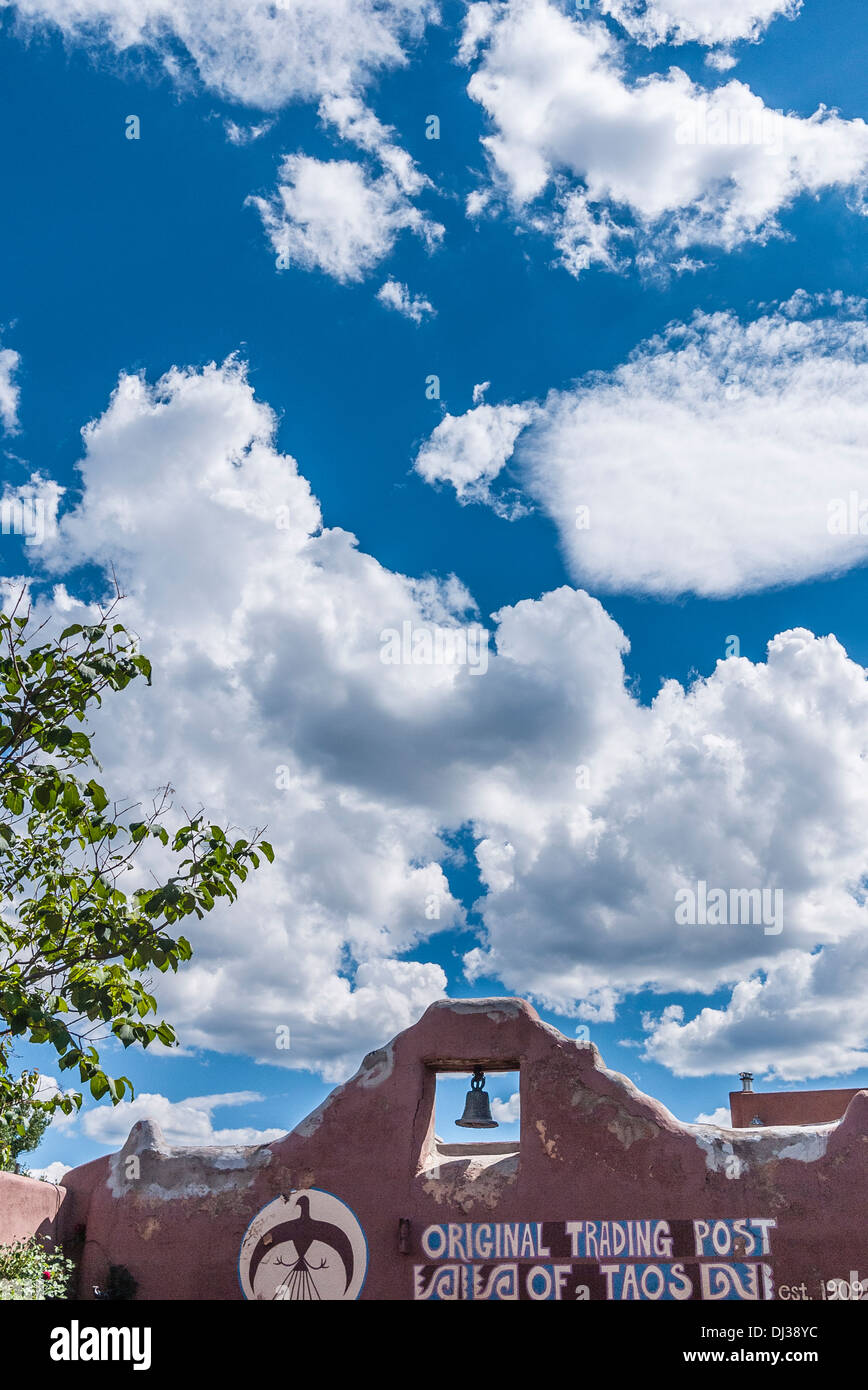 Détail de la partie supérieure de la façade avant de l'Original Trading Post de Taos, Nouveau Mexique avec bell dans adobe mur et ciel bleu. Banque D'Images