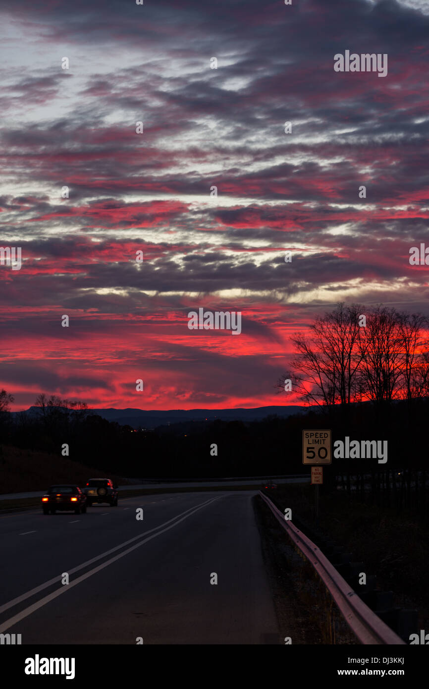 Coucher de soleil rouge dans un ciel partiellement nuageux, silhouetting arbres Banque D'Images