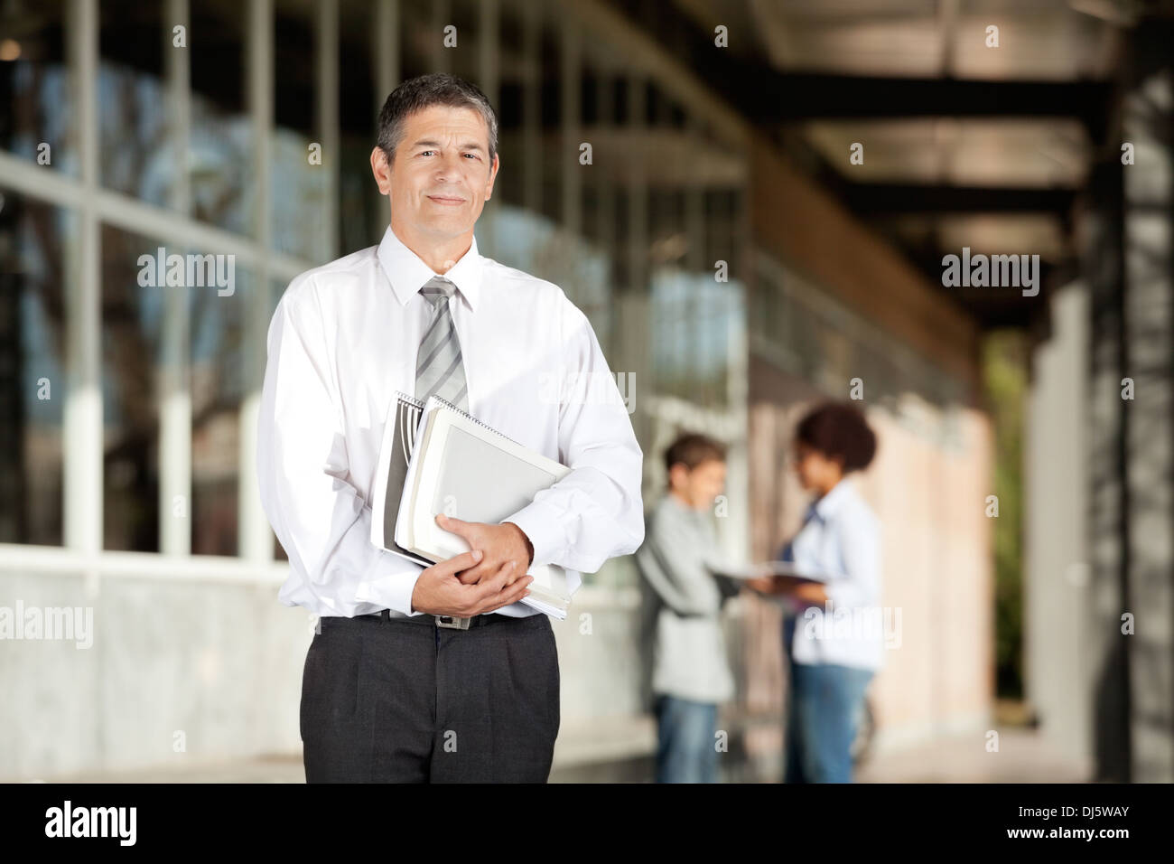 Teacher Holding Books tout en se tenant sur le campus Banque D'Images