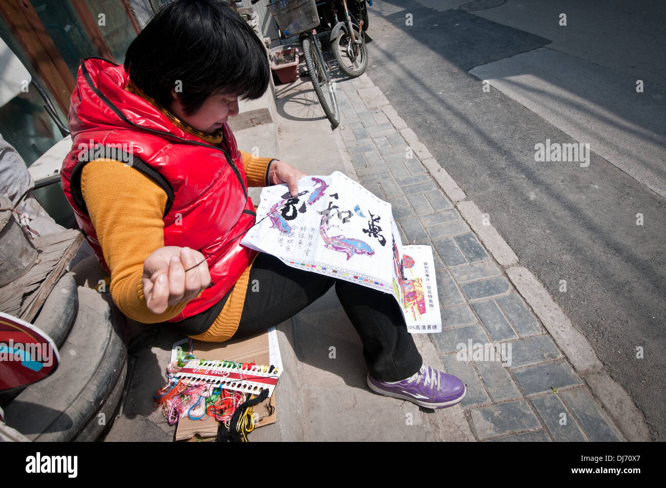 Femme faisant du point de croix dans la rue à Beijing, Chine Banque D'Images