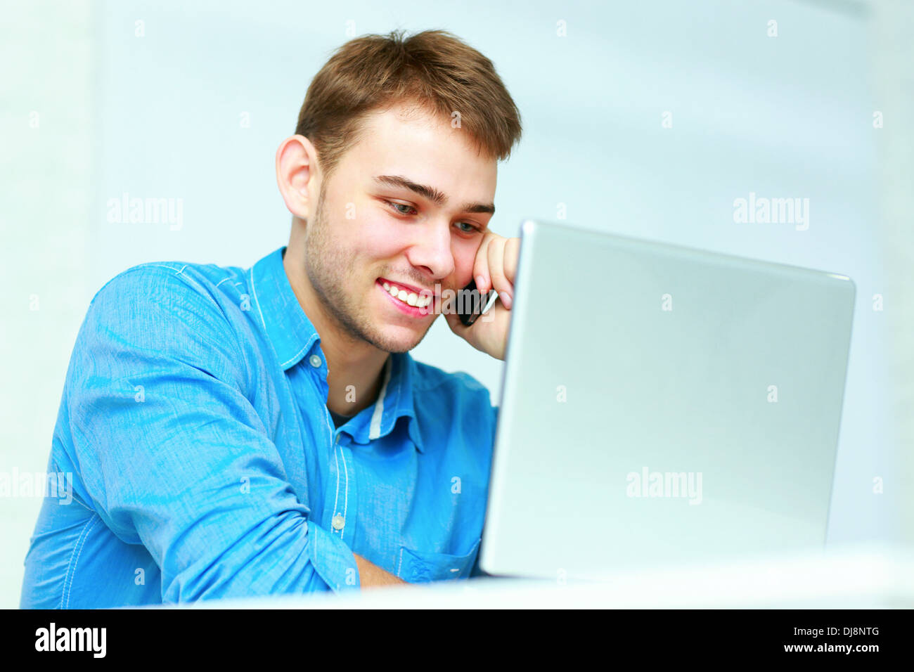 Jeune homme assis à la table avec ordinateur portable et parler au téléphone en fonction Banque D'Images