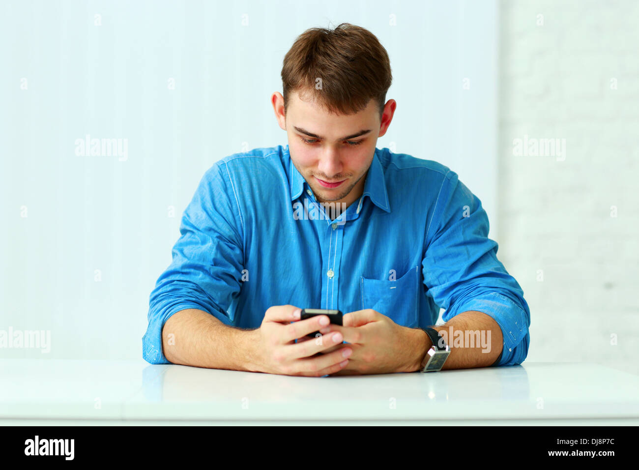 Young happy businessman assis à la table et en tapant sur smartphone in office Banque D'Images