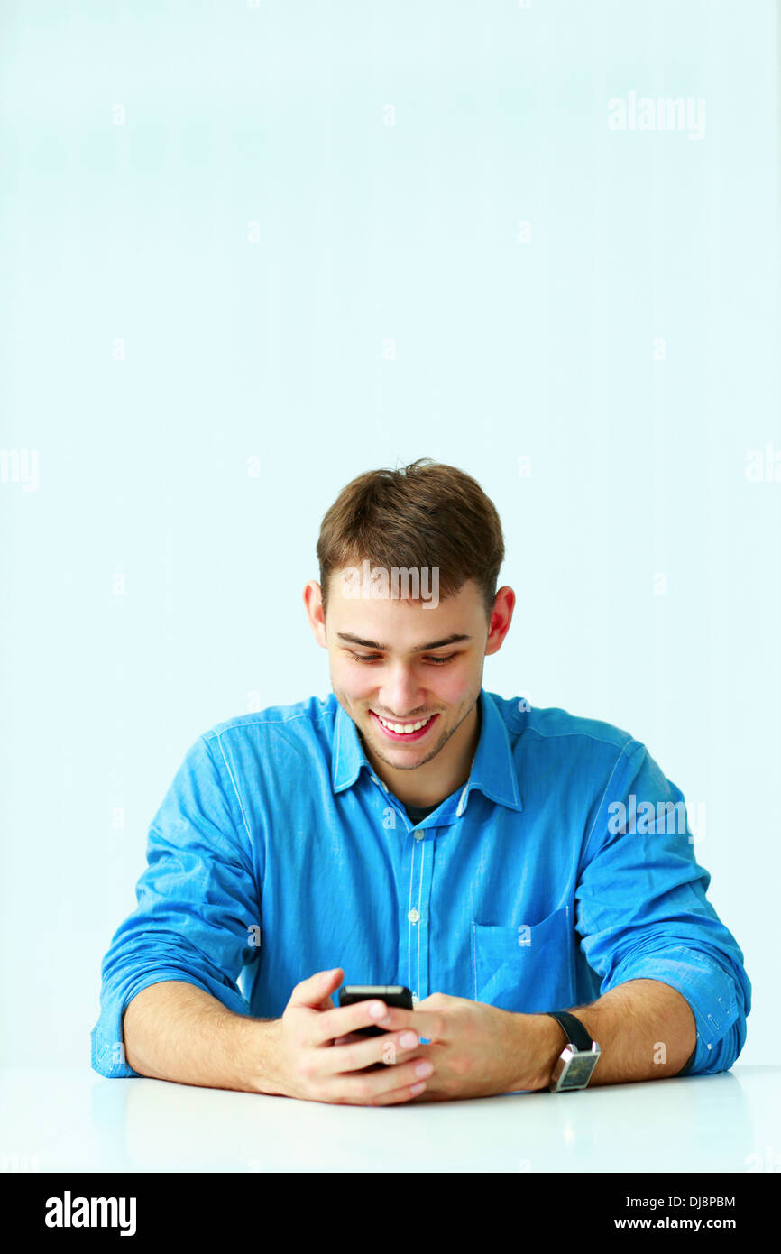 Young smiling businessman sitting at the table et looking at smartphone in office Banque D'Images