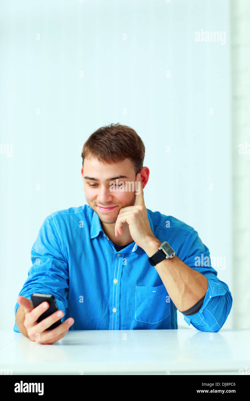 Young happy businessman sitting at the table et holding smartphone in office Banque D'Images