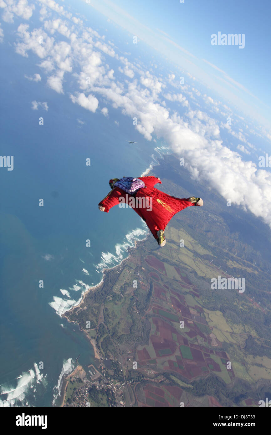 Ce parachutiste est dans un vol sur wingsuit champs verts dans le sens mer.Elle est ainsi plongée vers le bas et l'essai de la combinaison. Banque D'Images
