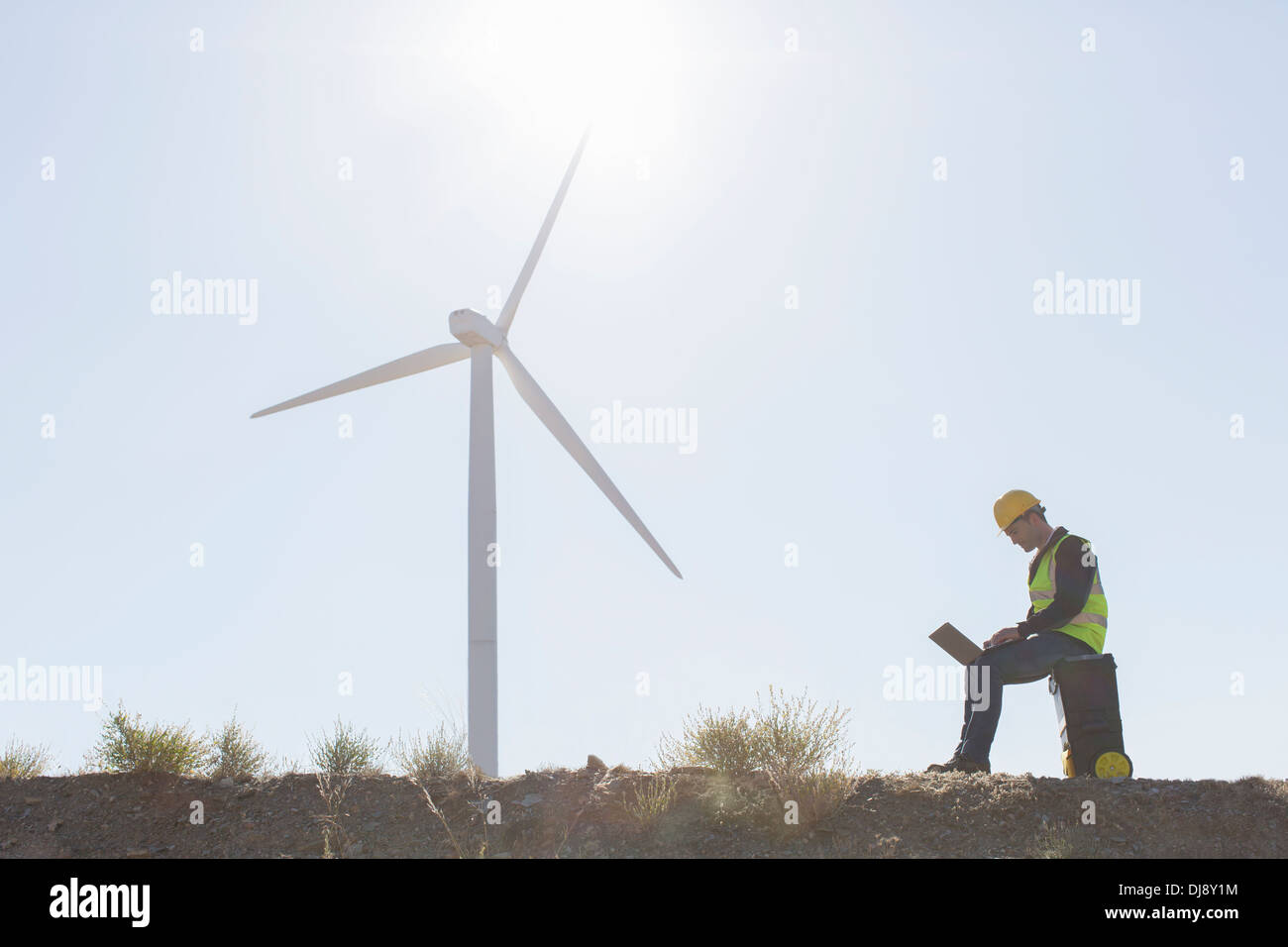 Worker using laptop by wind turbine in rural landscape Banque D'Images