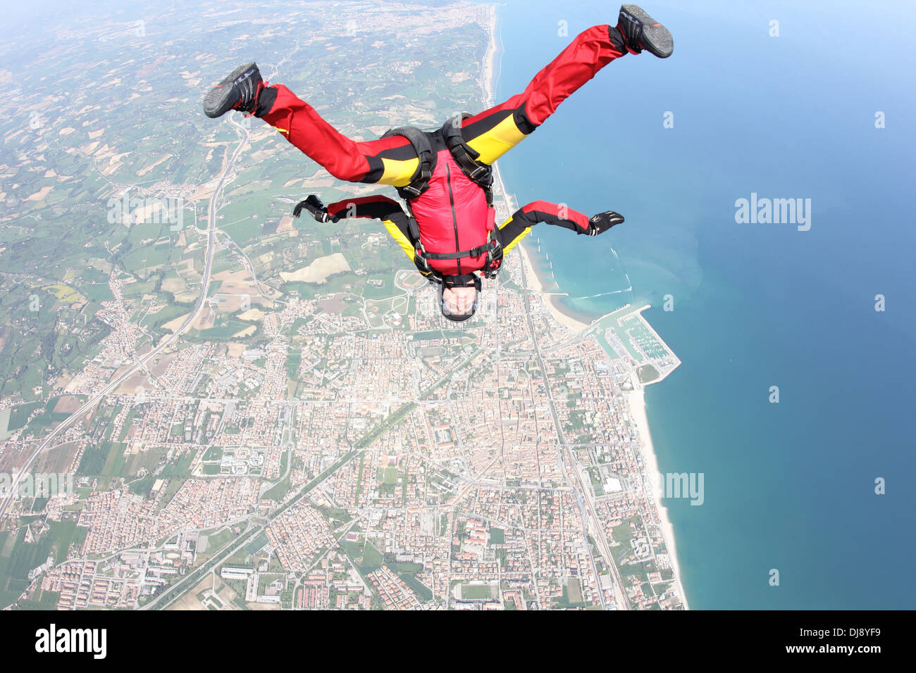 Cette femme parachutiste tombe gratuitement dans une position tête vers le bas sur une belle ligne de rivage. Elle a ainsi son plaisir à faire du sport. Banque D'Images