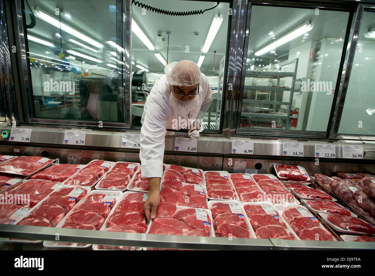 Employé hispanique portant la sécurité alimentaire les stocks nets de cheveux avec de la viande fraîche à un ministère à l'ouverture de l'entrepôt Costco store Banque D'Images