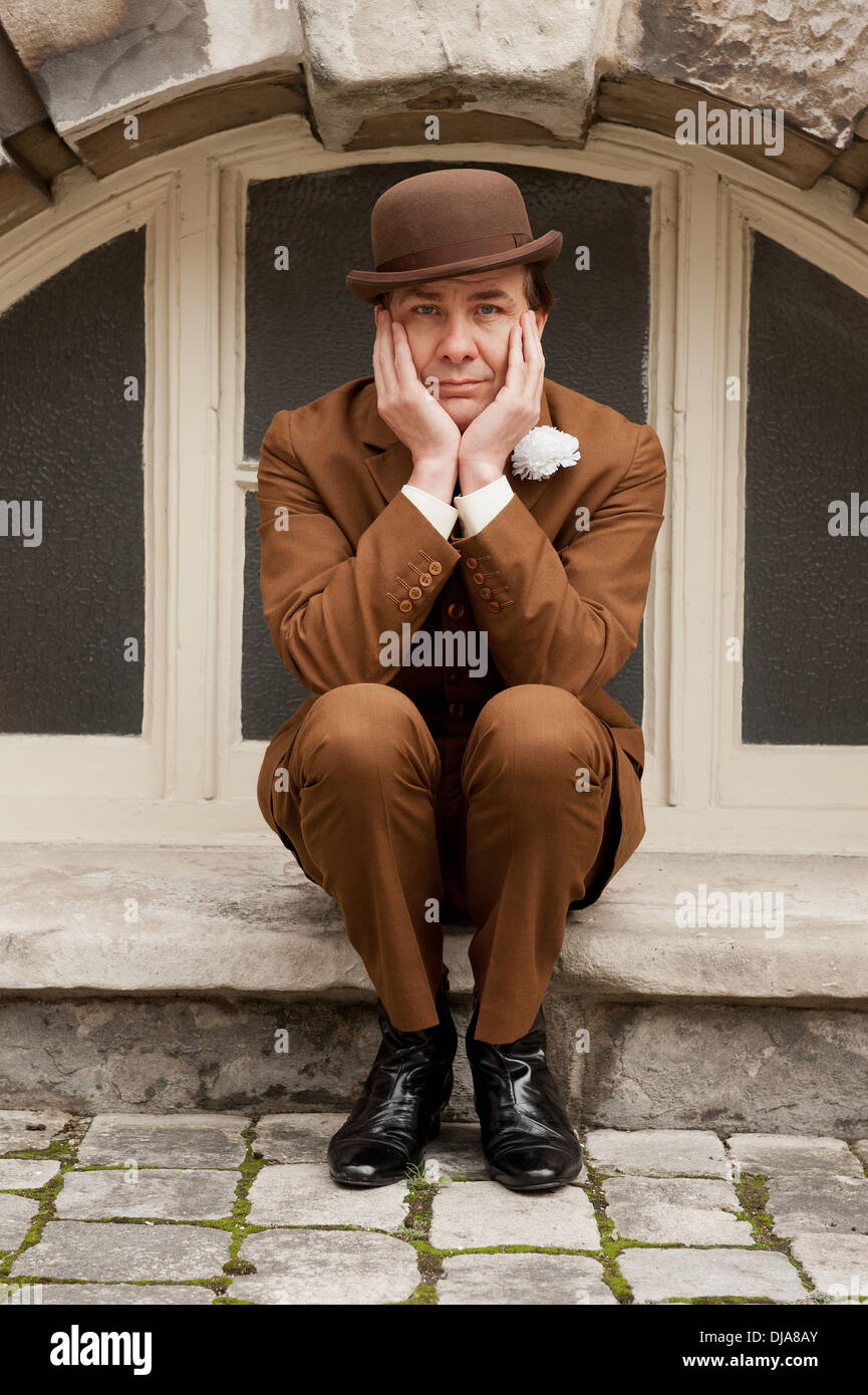 La ville de Gand dans dapper un costume marron et chapeau melon assis par une fenêtre en arc avec sa tête dans ses mains. Banque D'Images