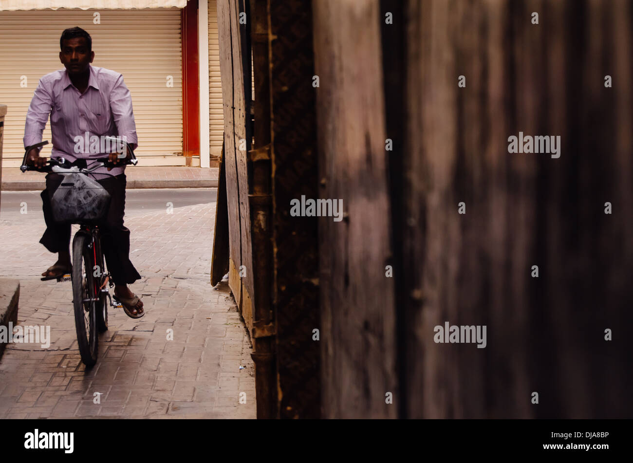 Un homme monté sur une bicyclette à travers les rues étroites de Deira. Dubaï, Émirats arabes unis. Banque D'Images