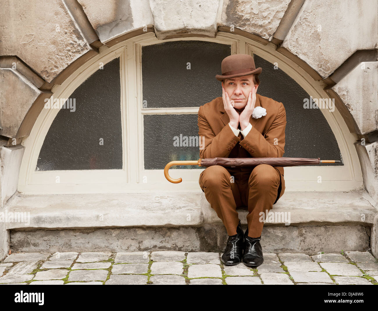 La ville de Gand dans dapper un costume marron et chapeau melon assis par une fenêtre en arc avec sa tête dans ses mains. Banque D'Images