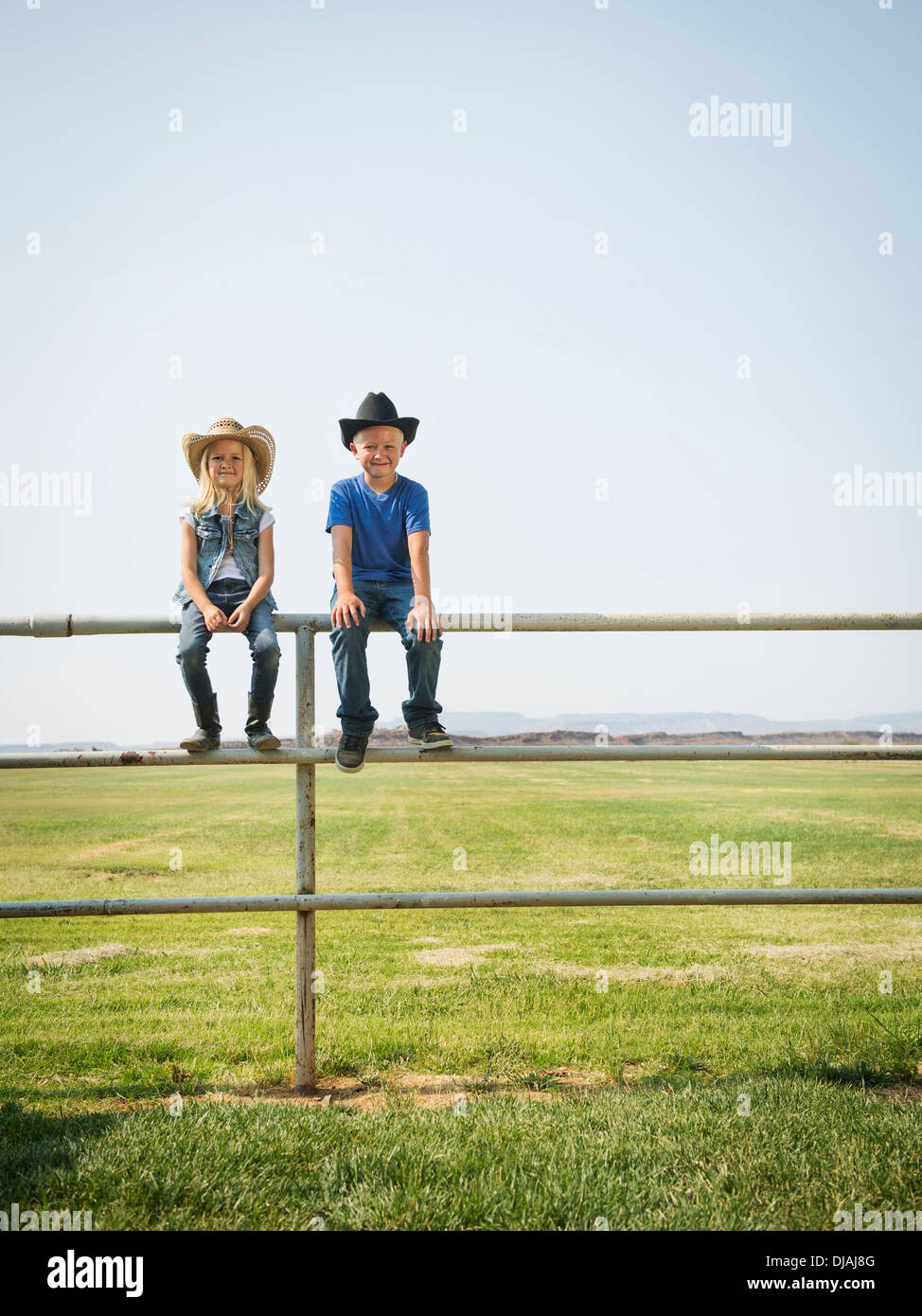 Caucasian children sitting on fence on farm Banque D'Images