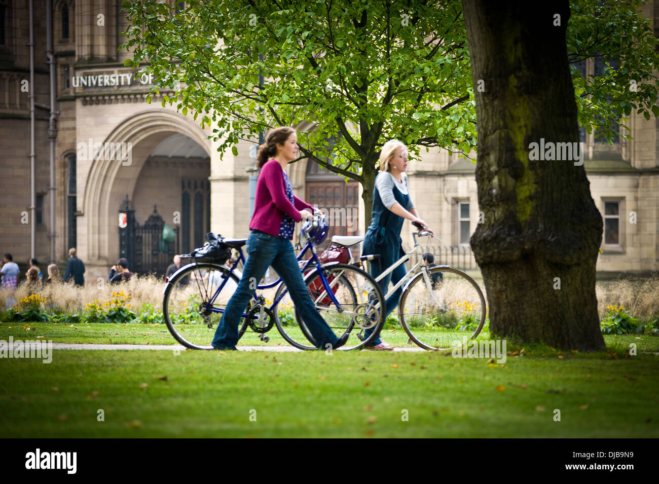 Les étudiants de l'université des femmes blanches poussant des vélos sur chemin en pelouse et d'arbres sur le campus de l'université Banque D'Images